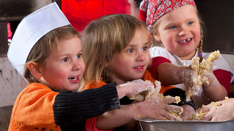 Drei kleine Kinder kneten gemeinsam Teig