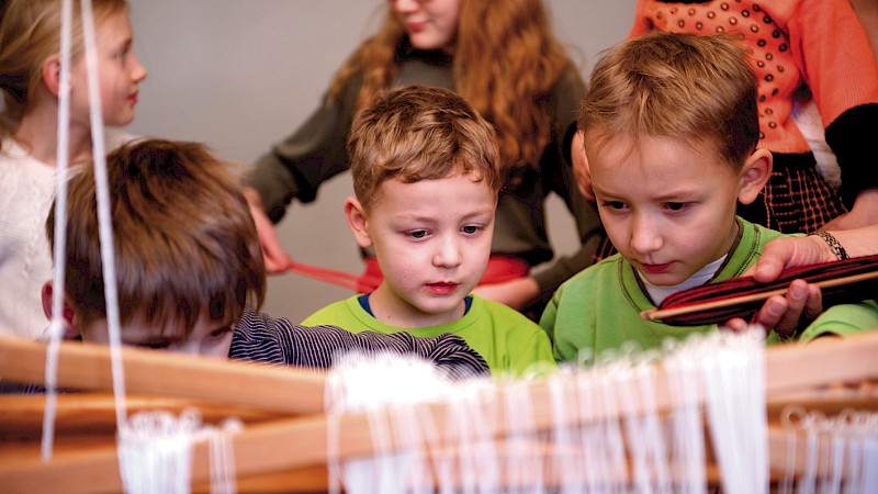 Mehrere Kinder arbeiten an einem Webstuhl