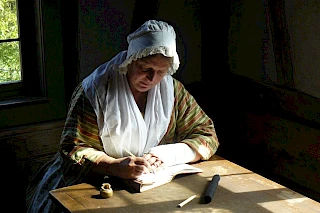 Landfrau in historischer Kleidung schreibt etwas in ein Buch