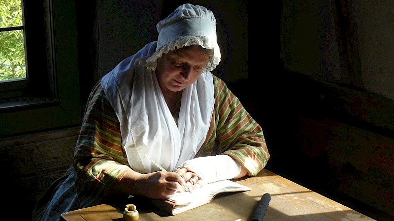 Landfrau in historischer Kleidung schreibt etwas in ein Buch