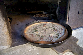 Pfanne mit dampfendem Rahmkuchen wird aus einem großen historischen Ofen geschaufelt