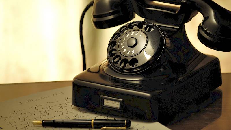 Schwarzes Wählscheibentelefon steht halb auf einem Zettel handgeschriebenen Notizen, man erkennt das Datum 3. Oktober 1912.