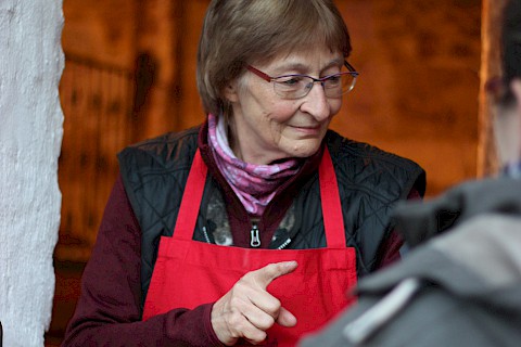 ältere Dame mit roter Schürze steht am Tresen