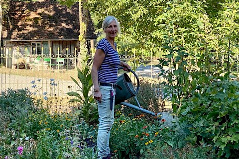 Eine Mitarbeiterin steht mit Gießkanne inmitten eines blühenden Blumenbeets