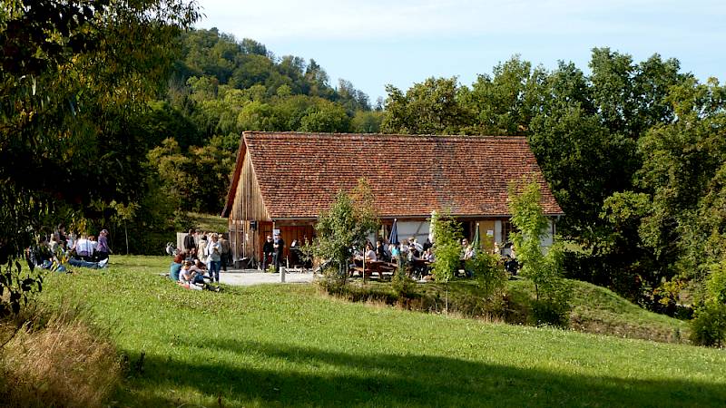 A historic building on a meadow with people at tables infront