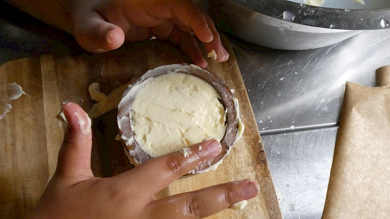 Zwei Kinderhände glätten ein Stück Butter in einer runden Form.