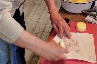 Erwachsenenhände streichen ein Stück Butter auf ein Papiertuch, daneben liegt ein fertiges Stück Butter