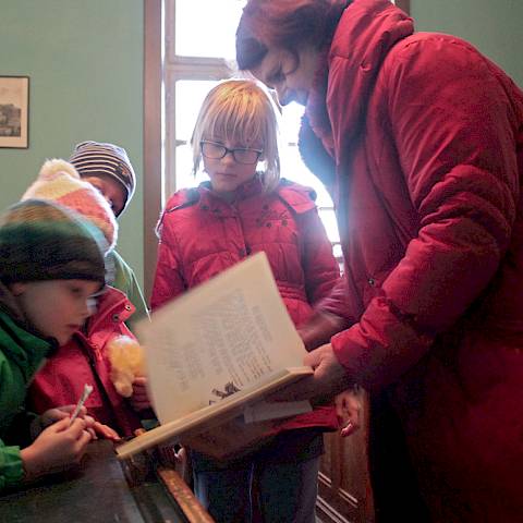 Eine Projektleiterin zeigt vier Kindern im alten Klassenzimmer ein Buch